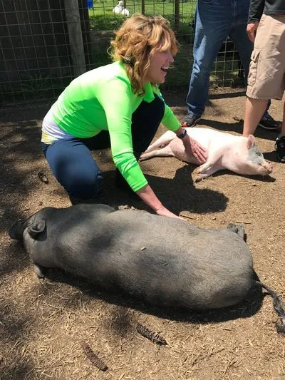 The founder, Sharon Marie, kneeling and petting two pigs outdoors.