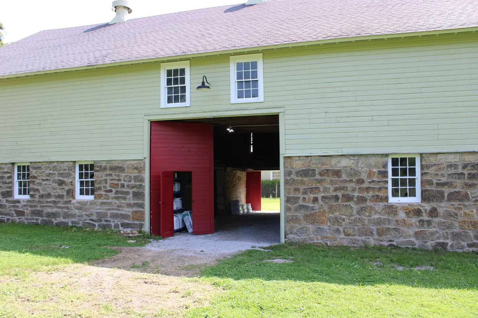 A green barn with red doors and stone base, sitting on the sanctuary grounds.